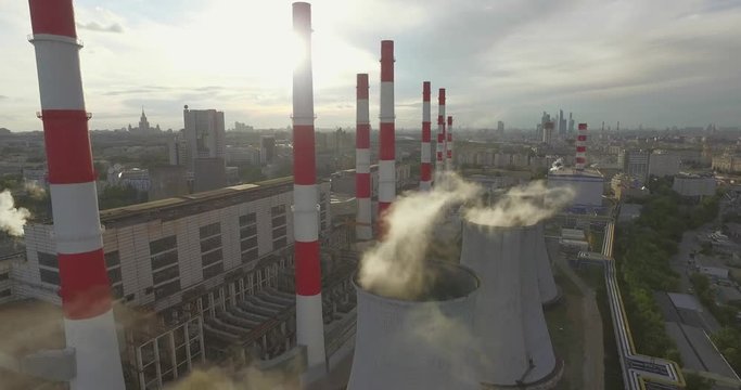 Aerial 4K shot of smoke or steam coming from an industrial chimney, Thermal power plant with huge cooling towers in city suburbs. Industry scenery, factory view, pollution and global warming concept