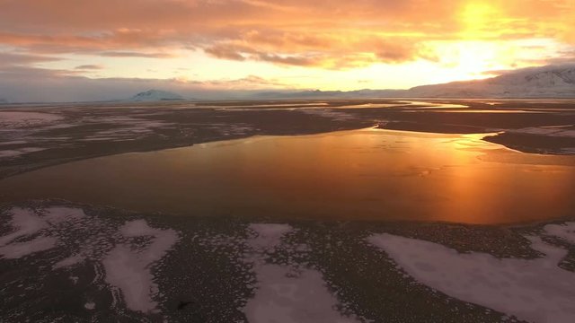 Aerial view flying backwards over frozen lake at sunset