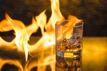 glass of whisky with ice on a black background and fire flames