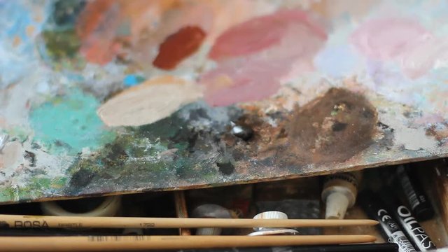 a colorful palette of oil paint on a plywood Board. The hand squeezes acrylic paint out of a tube.