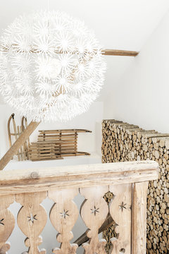 Balustrade of an old wooden chalet overlooking a log wall, old sleds and a white lamp