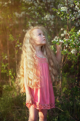 A beautiful little girl with long hair in a flowered garden