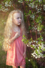 A beautiful little girl with long hair in a flowered garden