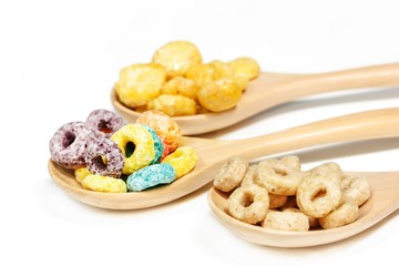 Variety of sugar cereals on wooden spoon isolated on white, selective focus