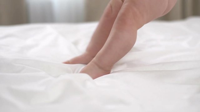 Little girl learns how to walk on the bed slow motion