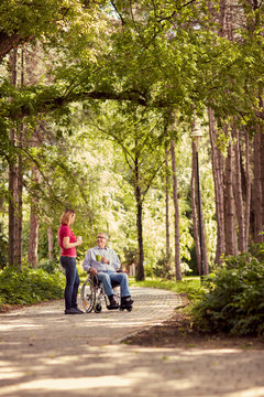 woman with her disabled happy father in wheelchair enjoying time together in the park.