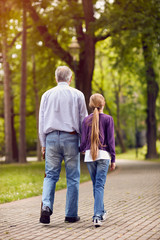 Girl and her grandfather holding hands on walk.