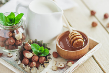 Honey in the wooden bowl, mint leaves, hazelnuts and jar with milk