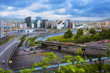 Cityscape of Oslo seen from above with skyscrapers view, bridges, green leafs in front of city and mountains in the background with cloudy sky