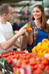 woman choosing pepper from salesman at street market.