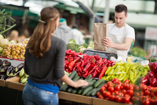 salesman measuring vegetables customer in grocery store.