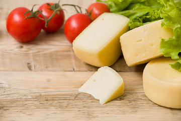 Cut cheese heads on wooden board served with tomatoes and fresh salad. Serving French homemade cheese. Food concept