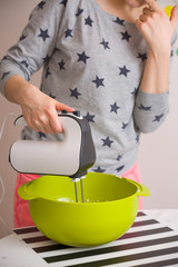 Young woman in long sleeve shirt with stars mixing and tasting dough for homemade muffins. Cooking and baking at home. Bright kitchenware and white mixer. Indoors.