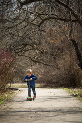 Fototapeta premium Cute kid boy riding his scooter and having fun in the park on a sunny day. Activities with children outdoors. Child on scooter. Lifestyle and active leisure concept.
