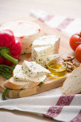 Variety of home made cheese and paprica and herbs, olive oil, olives and bread on a wooden board. brined curd white cheese with vegetables on the table