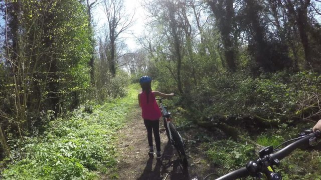 Parent and child walking through a forest with their mountain bikes, in first person view
