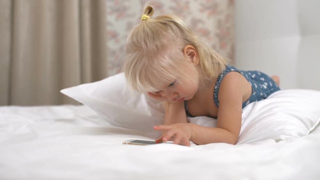 Little girl playing games on smartphone and lying on a soft pillow slow motion