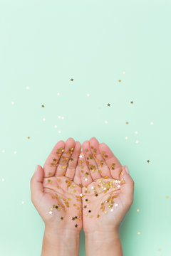 Top View On Woman's Hands Covered With Golden Stars Confetti On Light Blue Background. Christmas And Celebration Concept