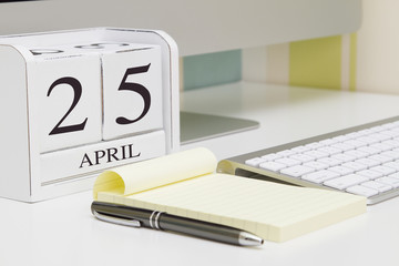 Cube shape calendar for April 25 and computer with white screen on table. 