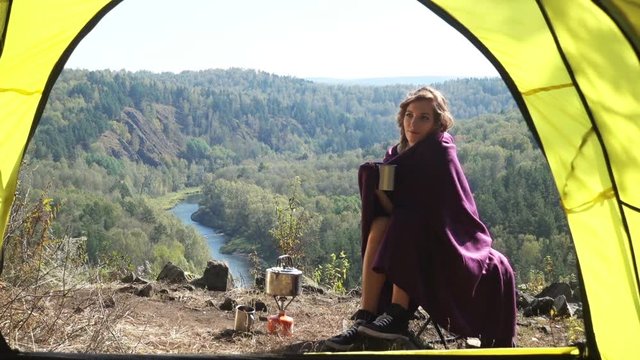 Young blonde woman tourist sitting on camping chair and drinking tea. Russia, Siberia, Salair