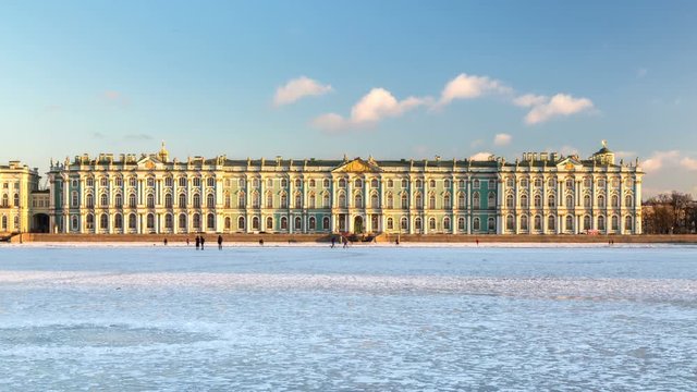 View of the Winter Palace in winter, people walk on the frozen river Neva, the rays of the setting sun illuminate the building of the Hermitage Museum. Saint-Petersburg, Russia.