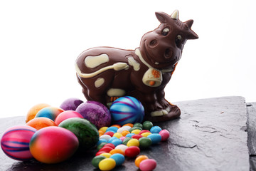 Chocolate Easter bunny and eggs with color ribbon bows on wooden background