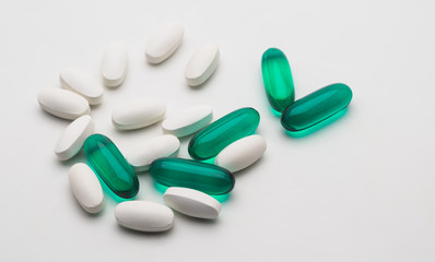 Green transparent capsules and white tablets on white background