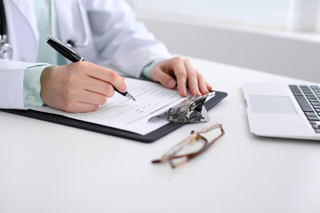 Close-up of a female doctor filling  out application form , sitting at the table in the hospital