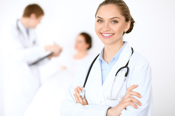 Cheerful smiling female doctor on the background with physician and his patient in the bed. High level and quality of medical service concept.