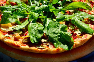 Rustic homemade delicious vegetarian pizza with arugula over black background, top view