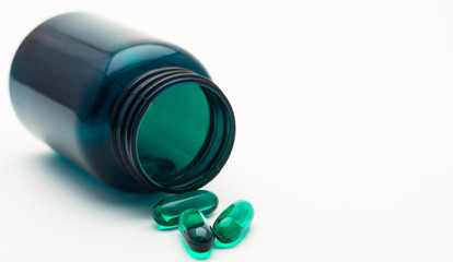 green transparent drug capsule in a green bottle on white background with copy space