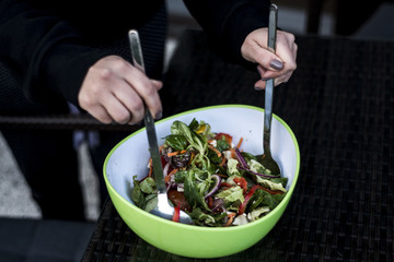 Delicious fresh healthy salad in a green bowl mixed by a woman hands with salad spoon food