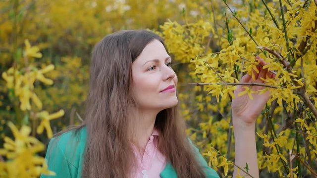 beautiful girl in green jacket smelling flower among yellow blossom tree