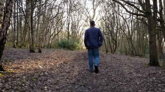 Forest walk; man walking into sunlight on a woodland path - rear following drone