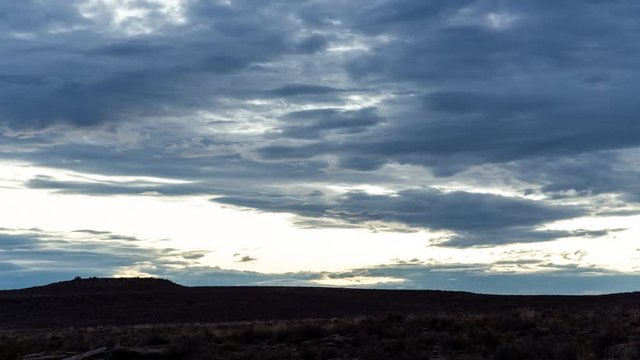 A static timelaspe at sunrise in a Karoo landscape setting as the dark landscape becomes brighter while the sun rises with dark dramatic clouds moving slowly 
