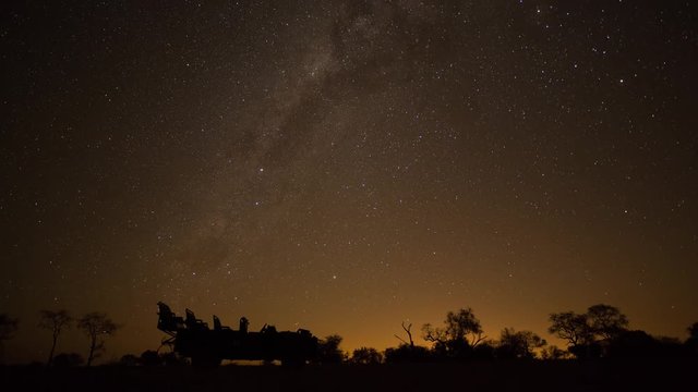 A static astro timelapse of 4x4 safari vehicle (jeep) silhouetted against the Milky Way and stars in a typical African bush landscape at night