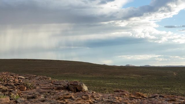 A static timelapse slowly tilting up to a stormy sky with rainy clouds and rocky foreground in a vast open landscape, typical Karoo, South Africa