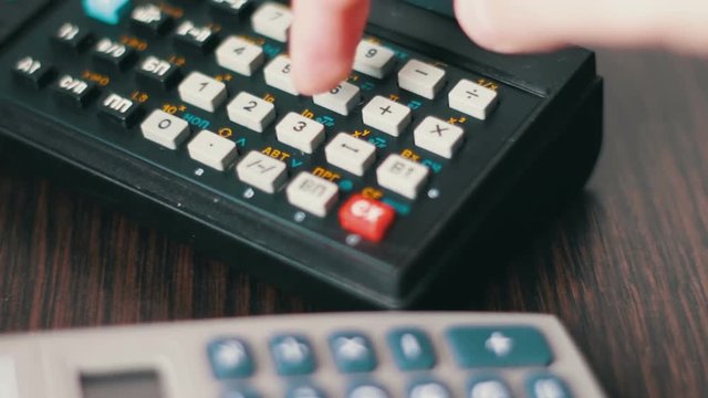 Hand operates old retro calculator at workstation