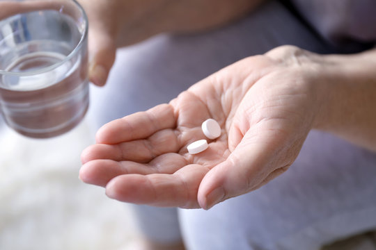 Senior woman with pills and glass of water at home, closeup
