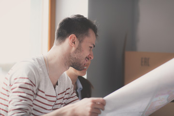 Fototapeta premium Young couple sitting on the floor and looking at the blueprint of new home