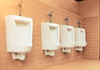 Row of white urinal for men on tile wall in toilet.