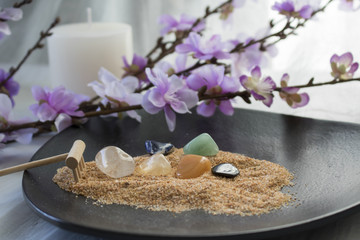 Obraz na płótnie Canvas Chakra stones in a bed of sand surrounded by flowers and a white candle.