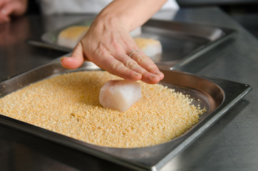 Fresh fish fillet cube being placed into breadcrumbs,before being pan fried.