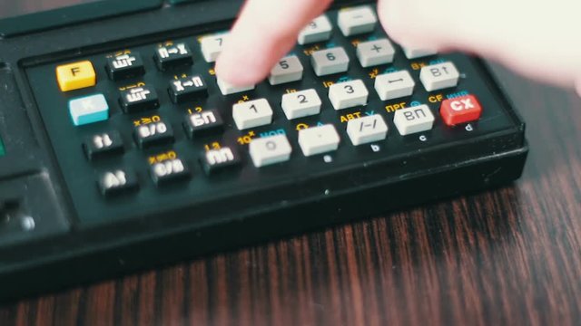 Hand operates old retro calculator at workstation