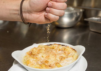 Cooked breadcrumbs being sprinkled onto oven bake macaroni cheese.