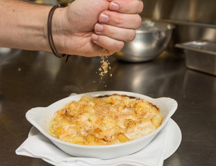 Cooked breadcrumbs being sprinkled onto oven bake macaroni cheese.