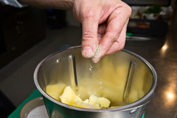Close up shot of a hand dropping black pepper onto fluffy peeled potatoes into a blender.