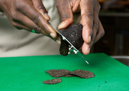 Expensive gourmet Black truffle being sliced thinly on a green cutting board