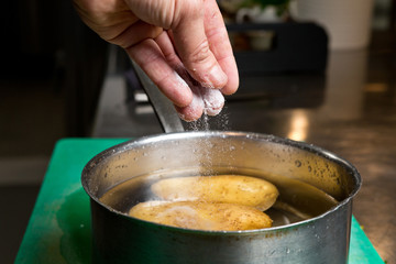 Salt being dropped into a pan of hot water containing potatoes