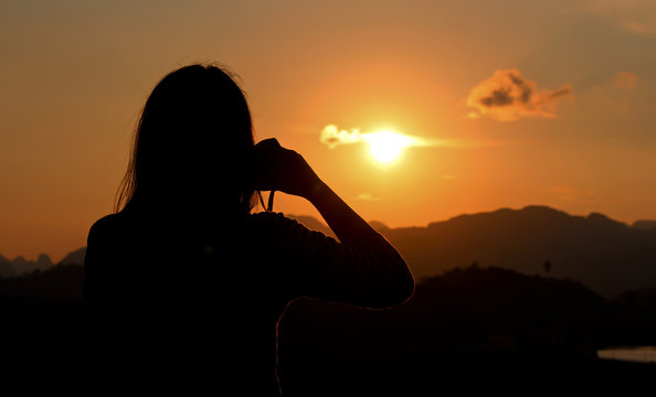 Asia woman photographer silhouette handing camera at sunset background.